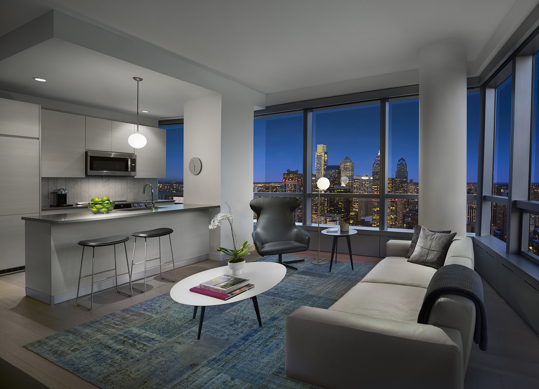 AKA University City living room with open kitchen and full-length window view of Philadelphia skyline at night 