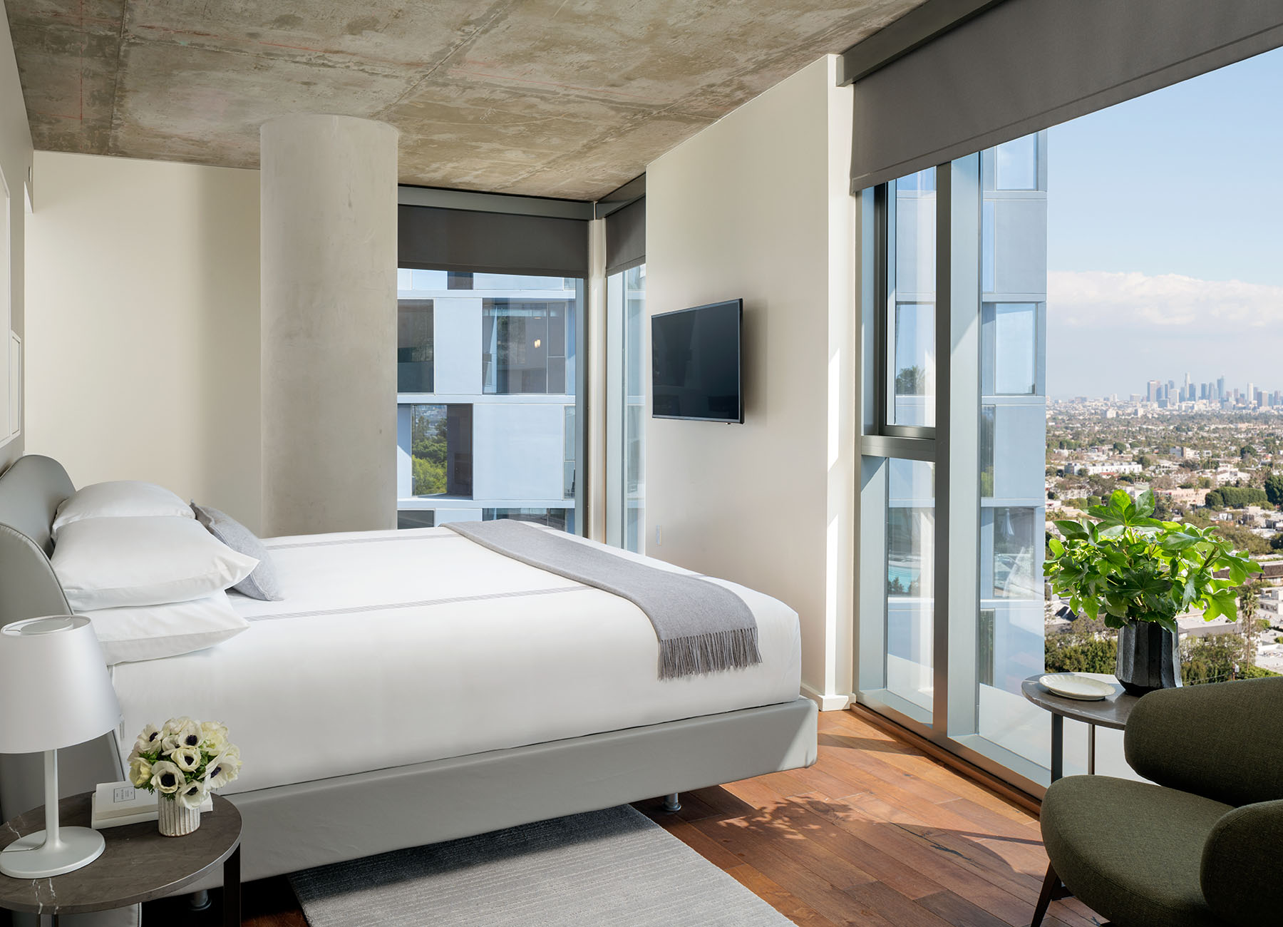 AKA West Hollywood apartment bedroom with concrete ceiling and king bed with large window view of city  