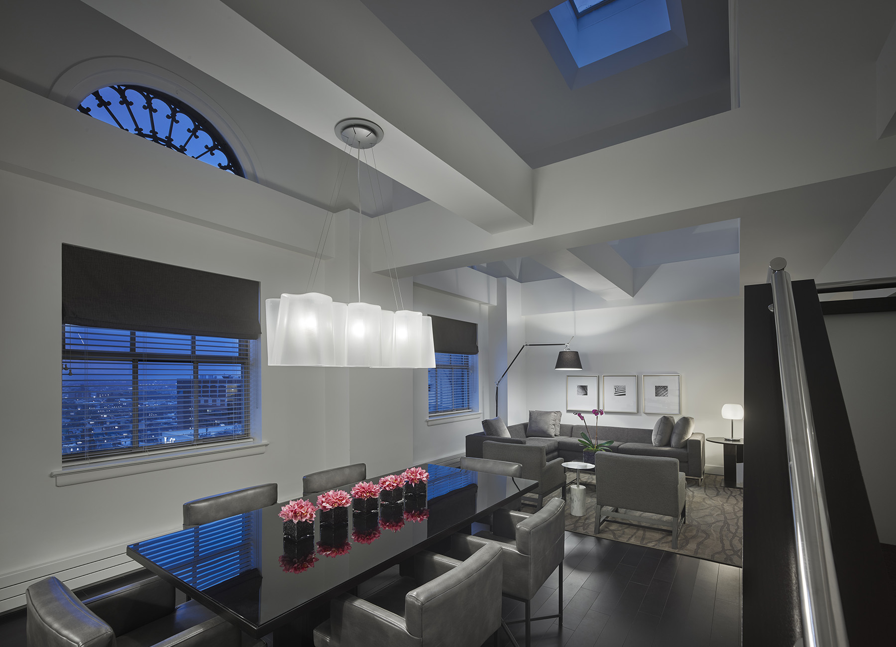 Philadelphia penthouse lounge with modern black and gray dining table for 8, stairs to second level, and arched windows showing dusk sky